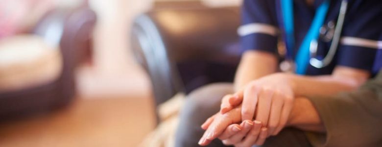 a female nurse is holding an elderly woman’s hand at home.