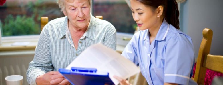 young home health nurse sitting at a table with an elderly woman talking